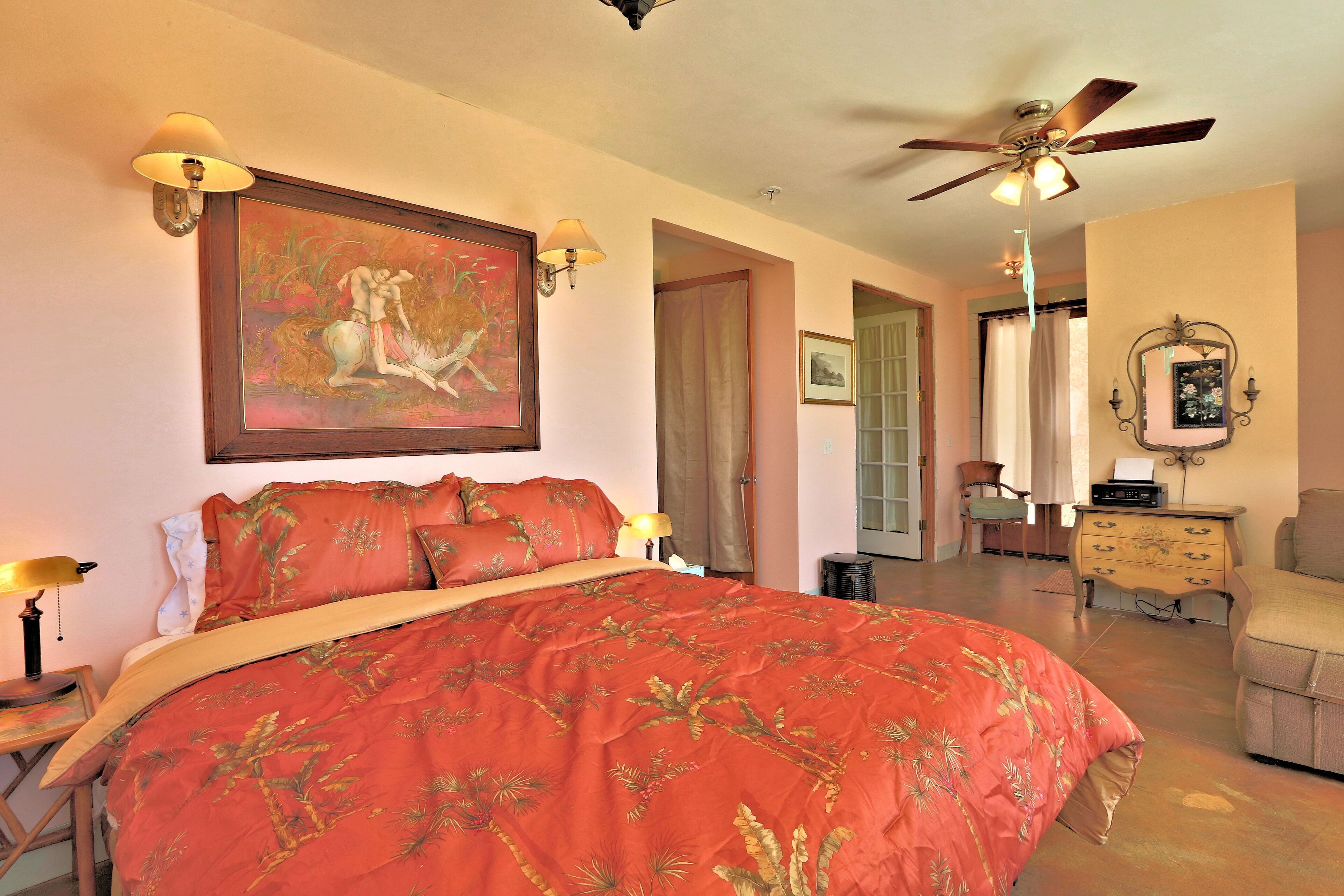 A bedroom with a large bed, a ceiling fan, a painting on the wall, and a dresser.