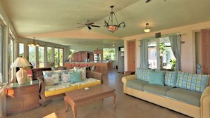A spacious living room with a sofa, coffee table, and a dining area with a kitchen in the background. - Puumoi Pink House, 3 bedroom home with sunrise and ocean view.10 minutes to Hilo (Papaikou)