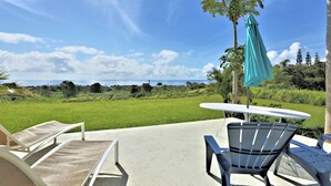 A patio with a table and chairs, a hanging umbrella, and a view of a grassy field and trees. - Puumoi Pink House, 3 bedroom home with sunrise and ocean view.10 minutes to Hilo (Papaikou)
