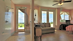 A spacious room with a large window, a ceiling fan, and a sofa. - Puumoi Pink House, 3 bedroom home with sunrise and ocean view.10 minutes to Hilo (Papaikou)