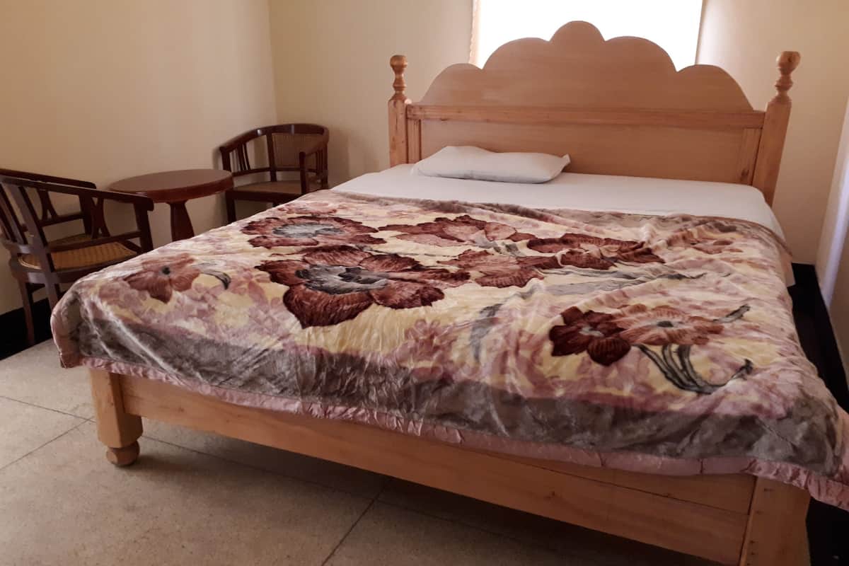 Una cama de madera con colcha estampada, cabecero de madera y una pequeña mesa con una silla.