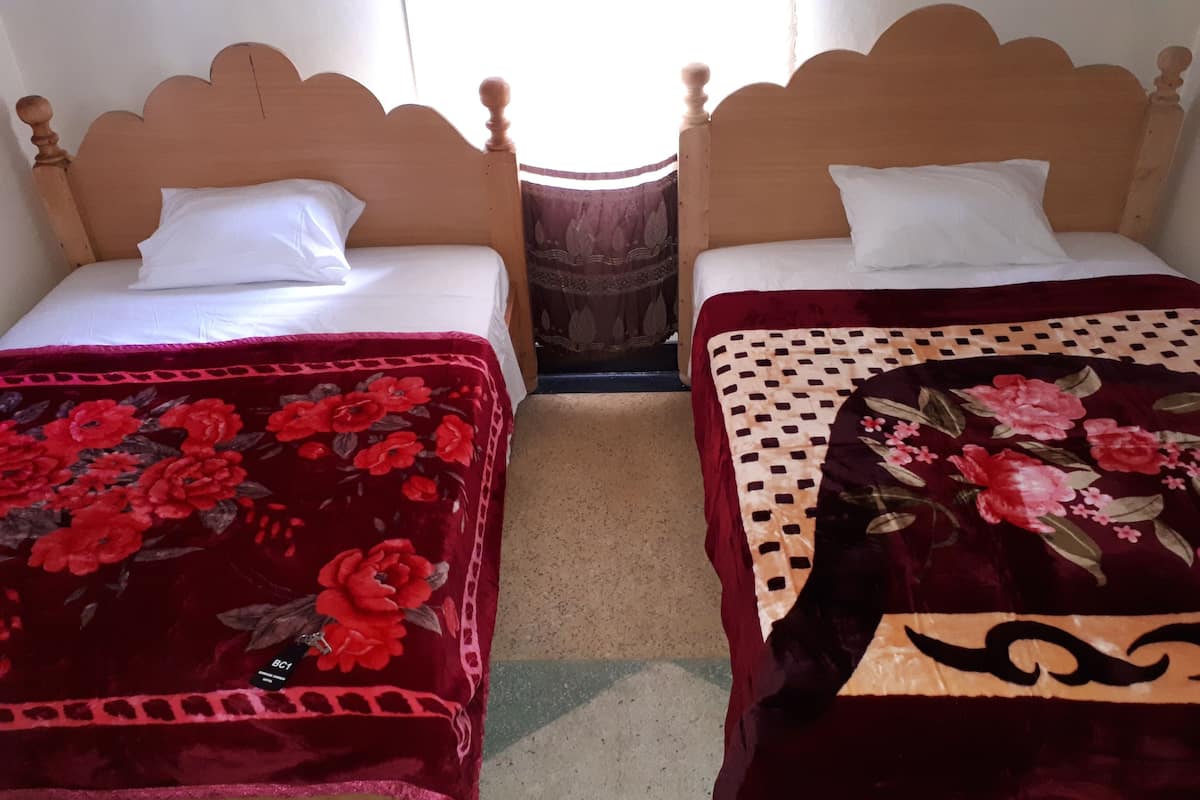 Dos camas de madera con almohadas blancas y colchas rojas estampadas con motivos florales.