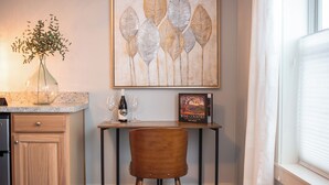 Une cuisine avec un meuble en bois, une table à manger avec deux verres à vin et une bouteille, et une œuvre d’art encadrée au-dessus de la table.
