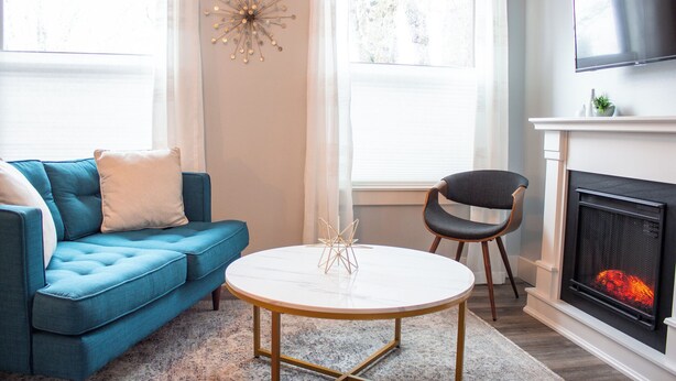 Un salon avec un canapé bleu, une table basse ronde, un fauteuil noir, une cheminée et un téléviseur fixé au mur.
