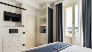 Habitación de hotel moderna con cama, televisor, minibar, armario y ventana con cortinas.