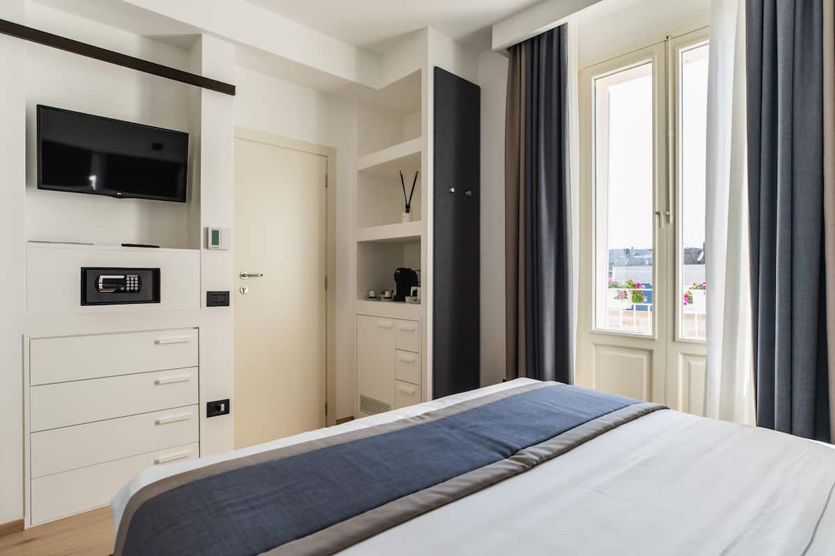 Habitación de hotel moderna con cama, televisor, minibar, armario y ventana con cortinas.