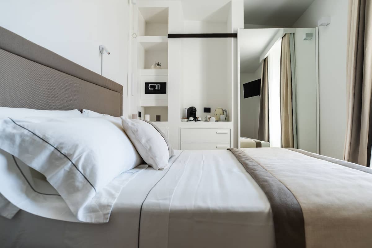 Una habitación de hotel con una cama, una mesita de noche, un espejo y un armario.