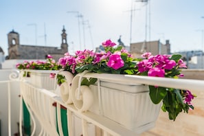 A balcony with white railings and a row of white flower pots containing pink flowers. - Dimora Maio (Monopoli)