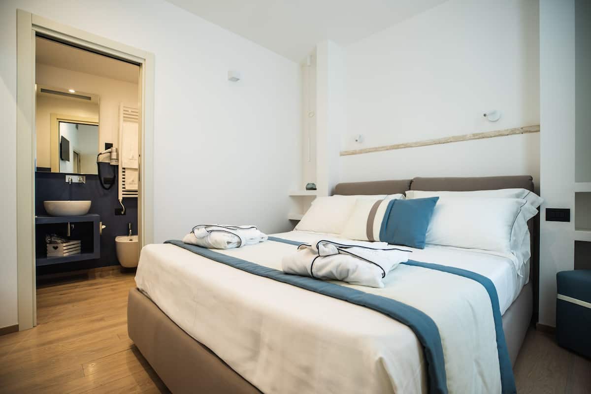 Una habitación de hotel moderna con una cama grande, una mesita de noche, un lavamanos integrado y un espejo.