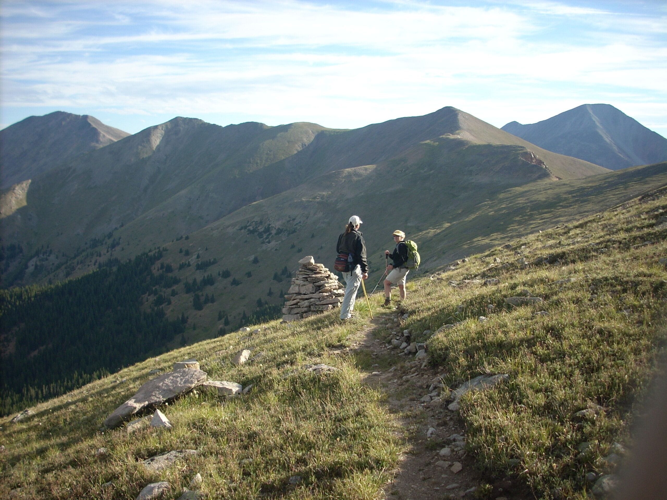 Un sentier de randonnée en montagne, avec deux randonneurs et un cairn de pierres.