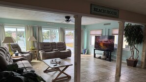 Un salón amplio con un sofá, una mesa de centro y un televisor. Un cartel dice "BEACH HOUSE".