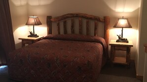 Une chambre d’hôtel avec une tête de lit en bois, deux tables de chevet avec des lampes et une couvre-lit à motifs floraux.
