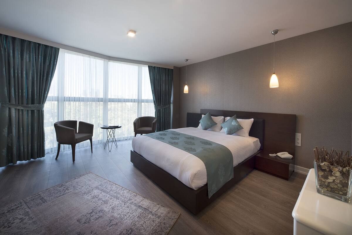 A modern hotel room with a large bed, two chairs, a small table, and a nightstand with a phone.