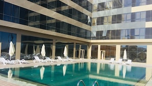 A swimming pool with lounge chairs and umbrellas, surrounded by a modern building with large windows. - New Suites (Istanbul)