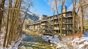 A multi-story building with balconies and a river in the foreground. - Aspen Riverfront Luxury 3BR, Top Floor, Pool, Hot Tub, Gym, 7Min Walk to Gondola (Aspen)