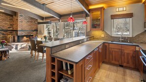 A spacious kitchen with a large island, wooden cabinets, and a brick fireplace. - Aspen Riverfront Luxury 3BR, Top Floor, Pool, Hot Tub, Gym, 7Min Walk to Gondola (Aspen)