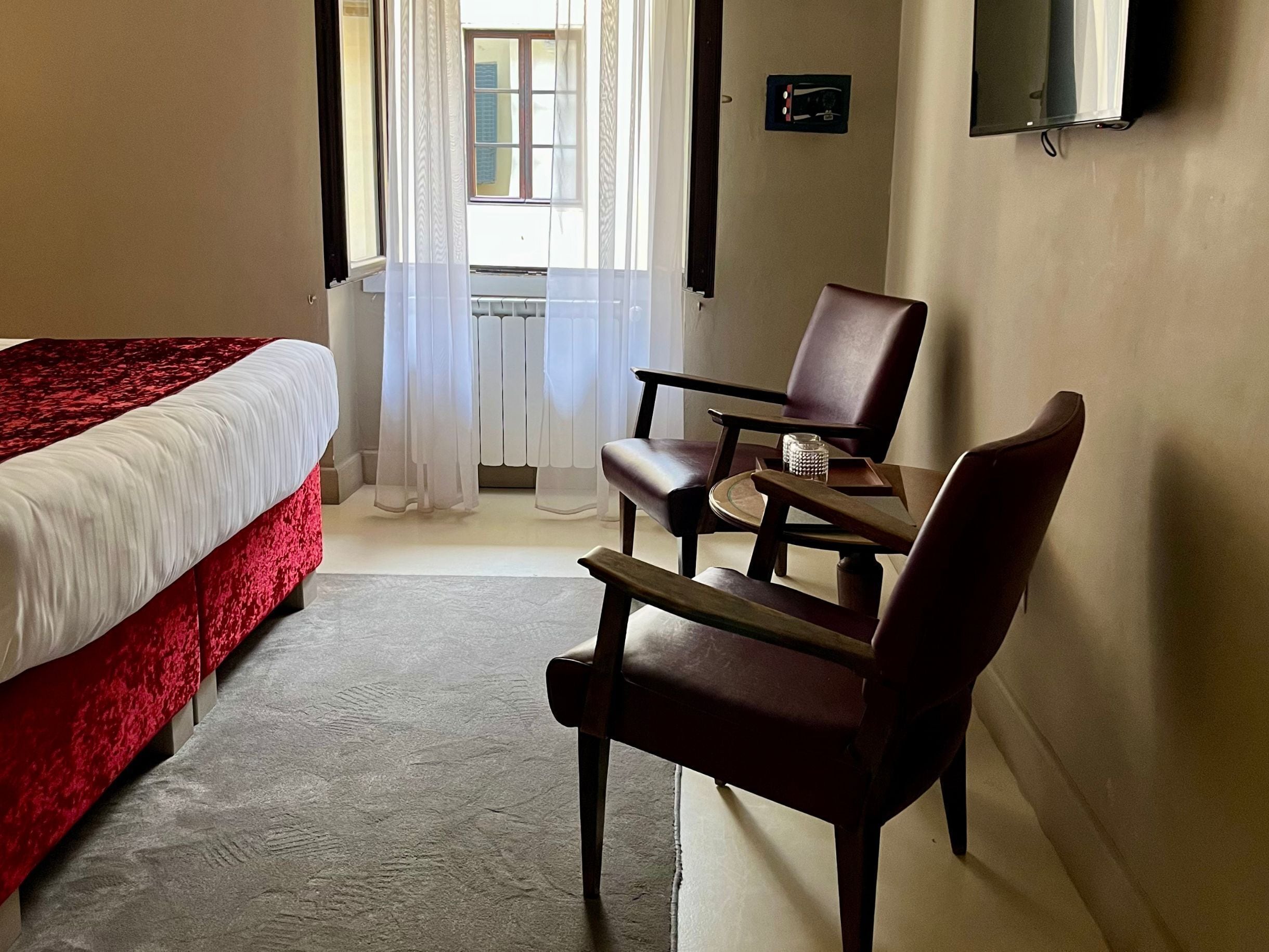 Une chambre d’hôtel avec un lit, une chaise, une petite table et un téléviseur fixé au mur.