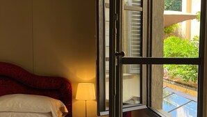 A hotel room with a bed, a bedside lamp, and a window with a view of greenery and a building. - Numa Florence  Palazzo San Niccolò (Florence)