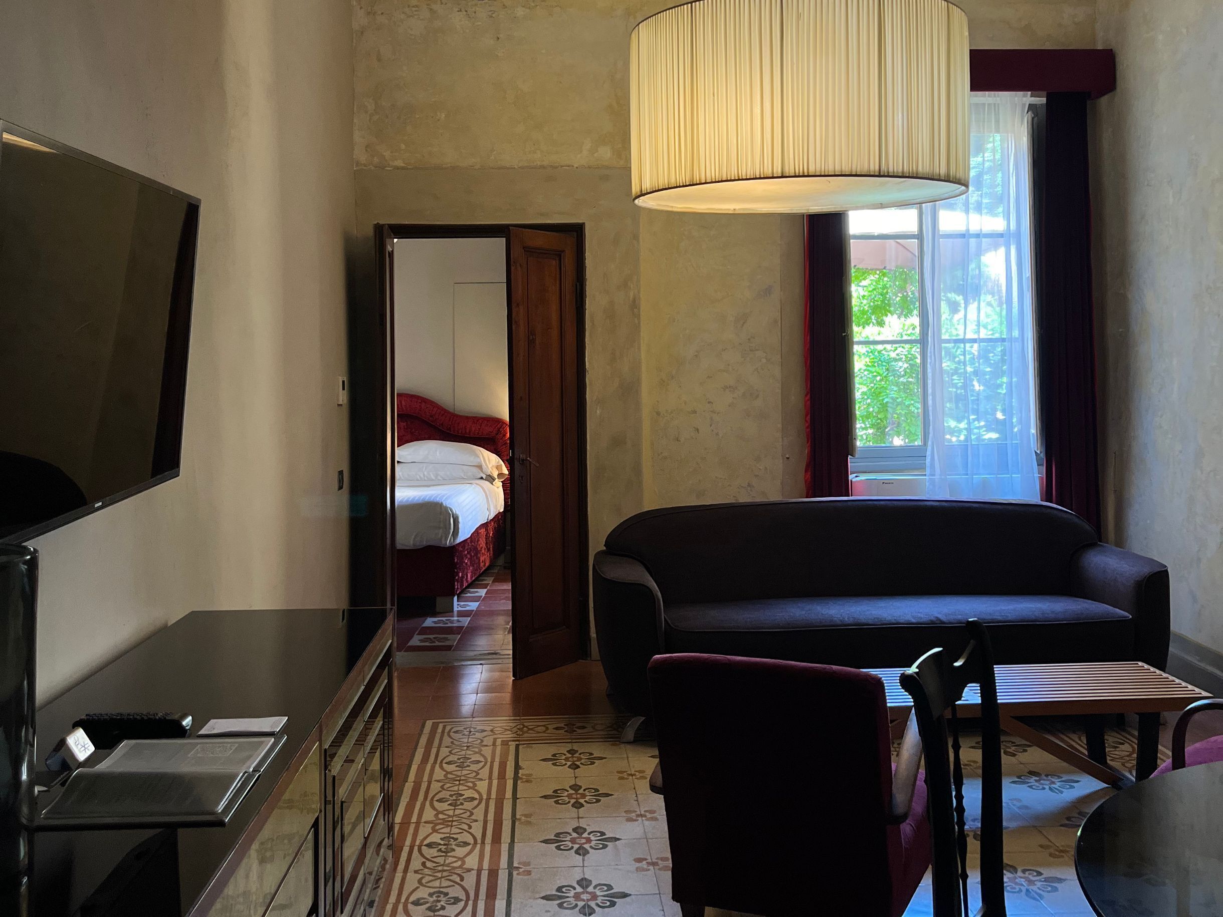 Habitación de hotel con cama, televisor, sofá, mesa de comedor y ventana con cortinas.