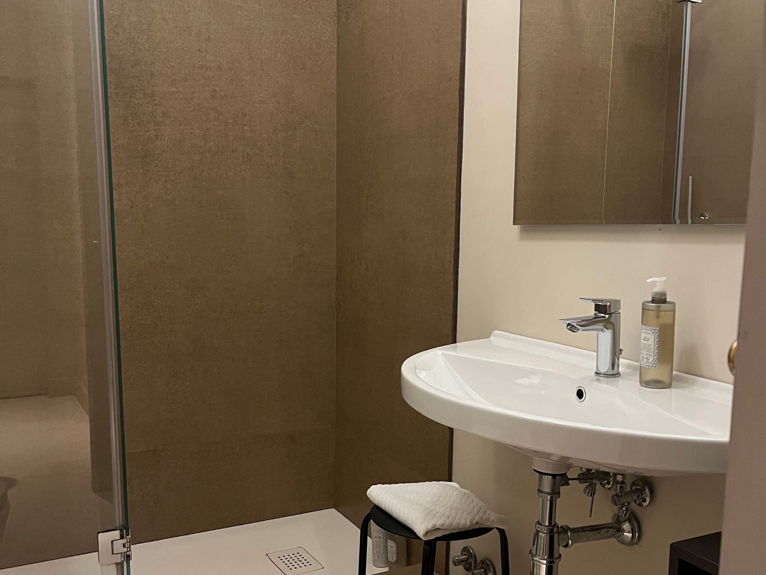 Een badkamer met een wit wastafelmeubel, een spiegel en een douchecabine van glas.