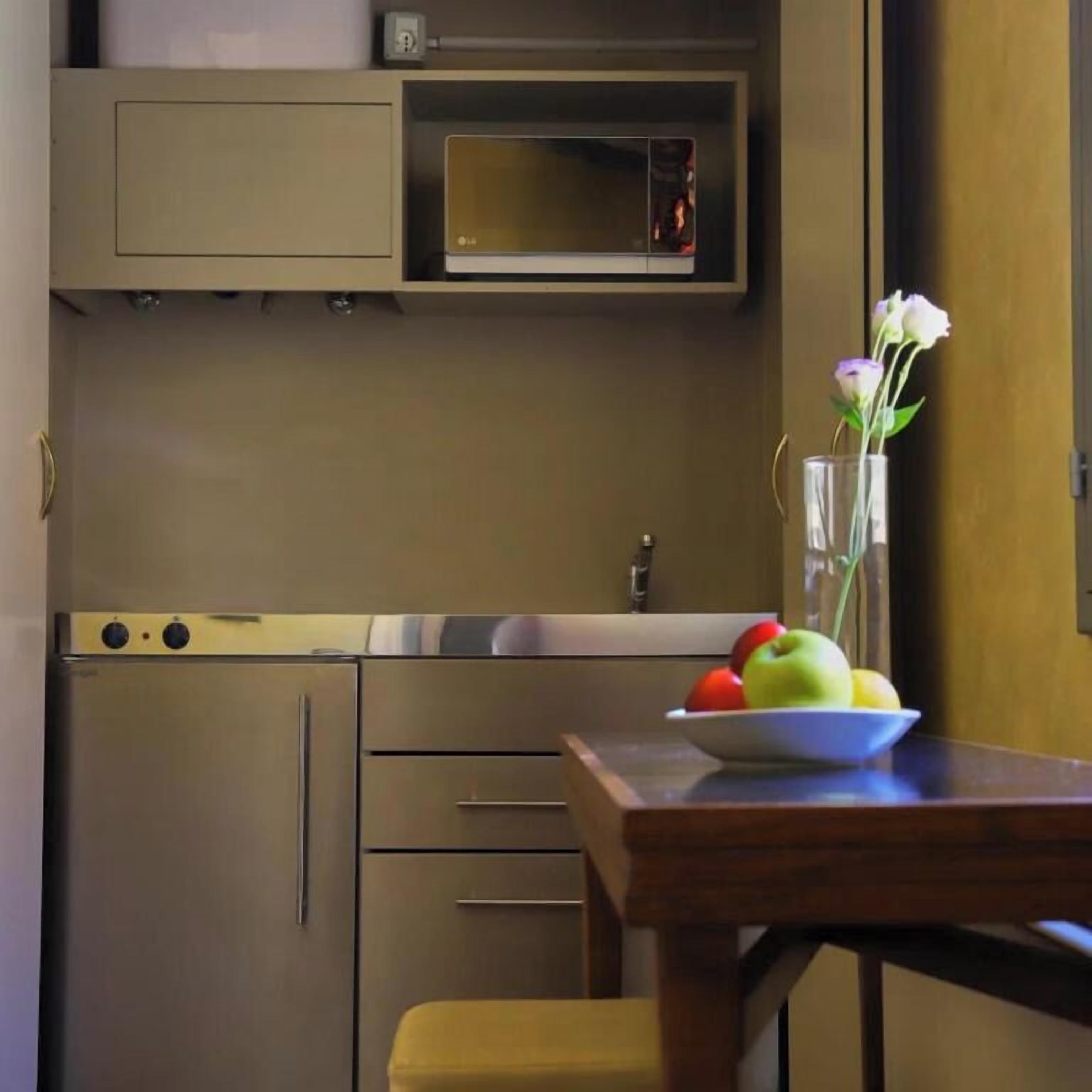 A compact kitchen with a microwave, a bowl of fruit, and a vase with flowers on a table.