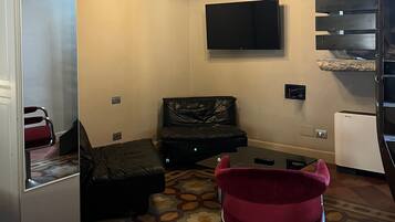 Un espacio habitable compacto con un sofá, un sillón rojo, un televisor de pantalla plana en la pared y un refrigerador pequeño.