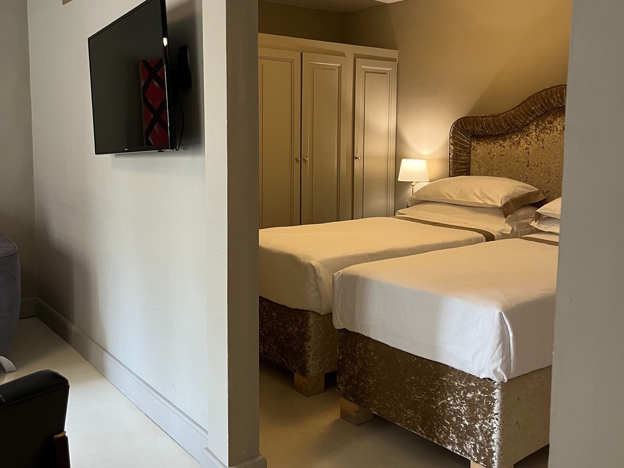 Una camera d'albergo con due letti, un armadio, una televisione e una lampada.