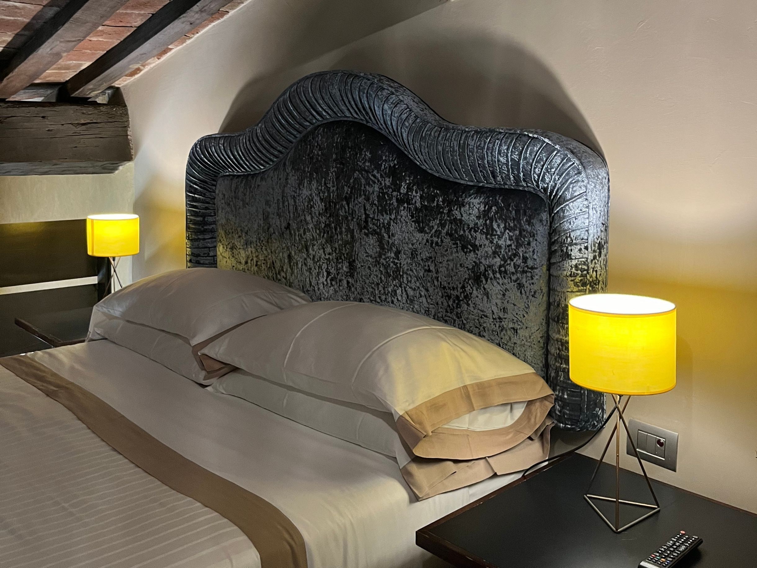 A bed with a headboard, two bedside lamps, and a remote control on a nightstand.