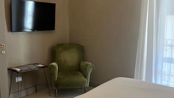 Une chambre d’hôtel avec un lit, un fauteuil vert, une petite table avec une lampe et un téléviseur à écran plat fixé au mur.