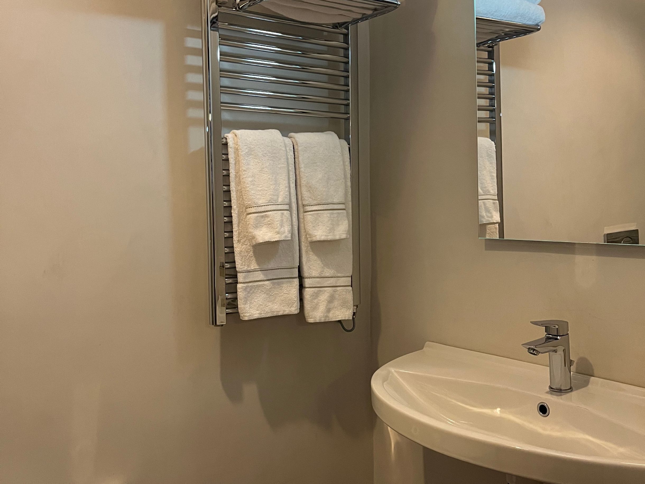 Ein Badezimmer mit einem weißen Waschbecken, einem Spiegel und einem Handtuchhalter mit zwei Handtüchern.