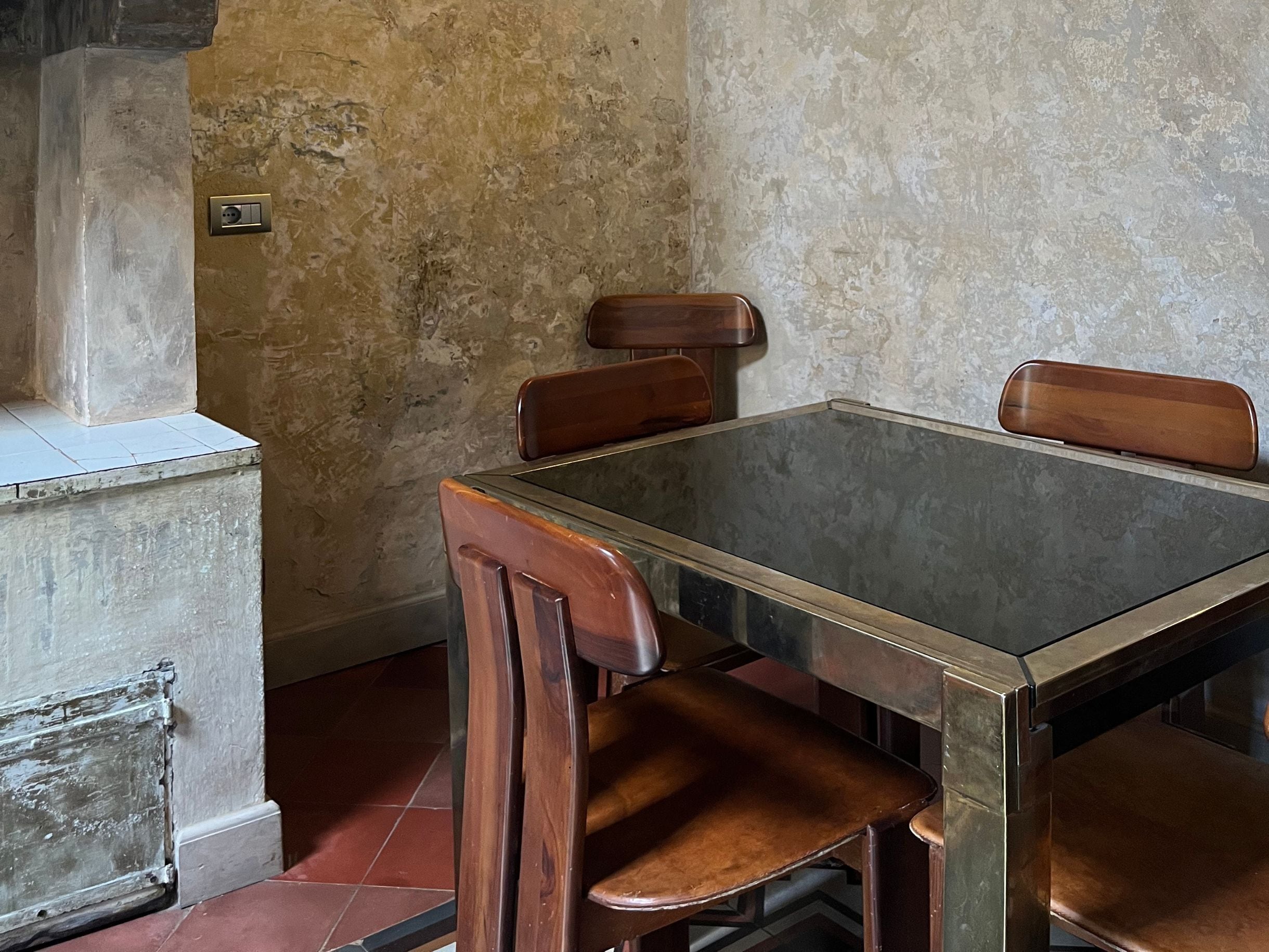 Una mesa de comedor con cuatro sillas de madera, suelo de baldosas y pared con textura.