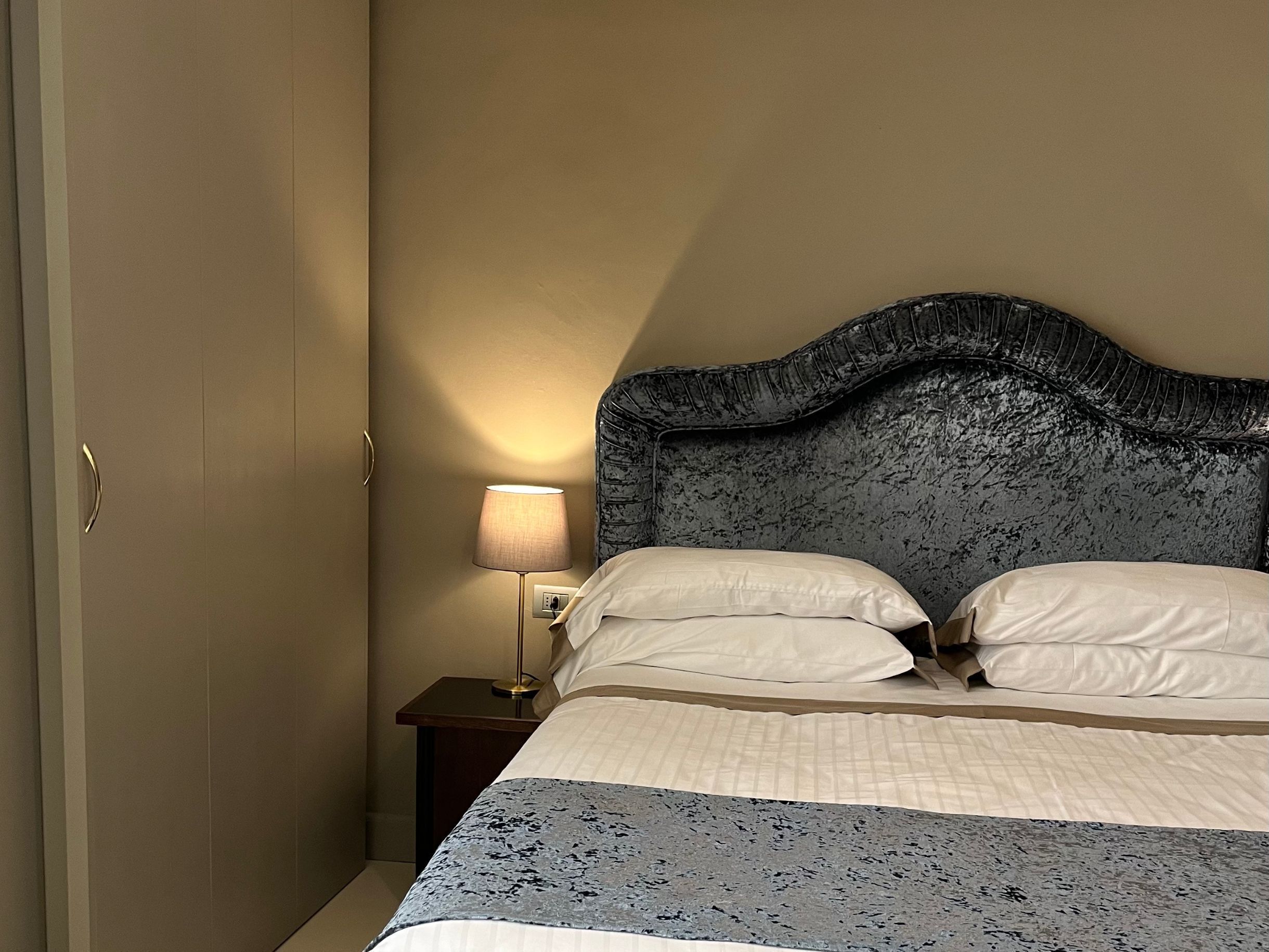 A hotel room with a bed, a nightstand, a lamp, and a door.