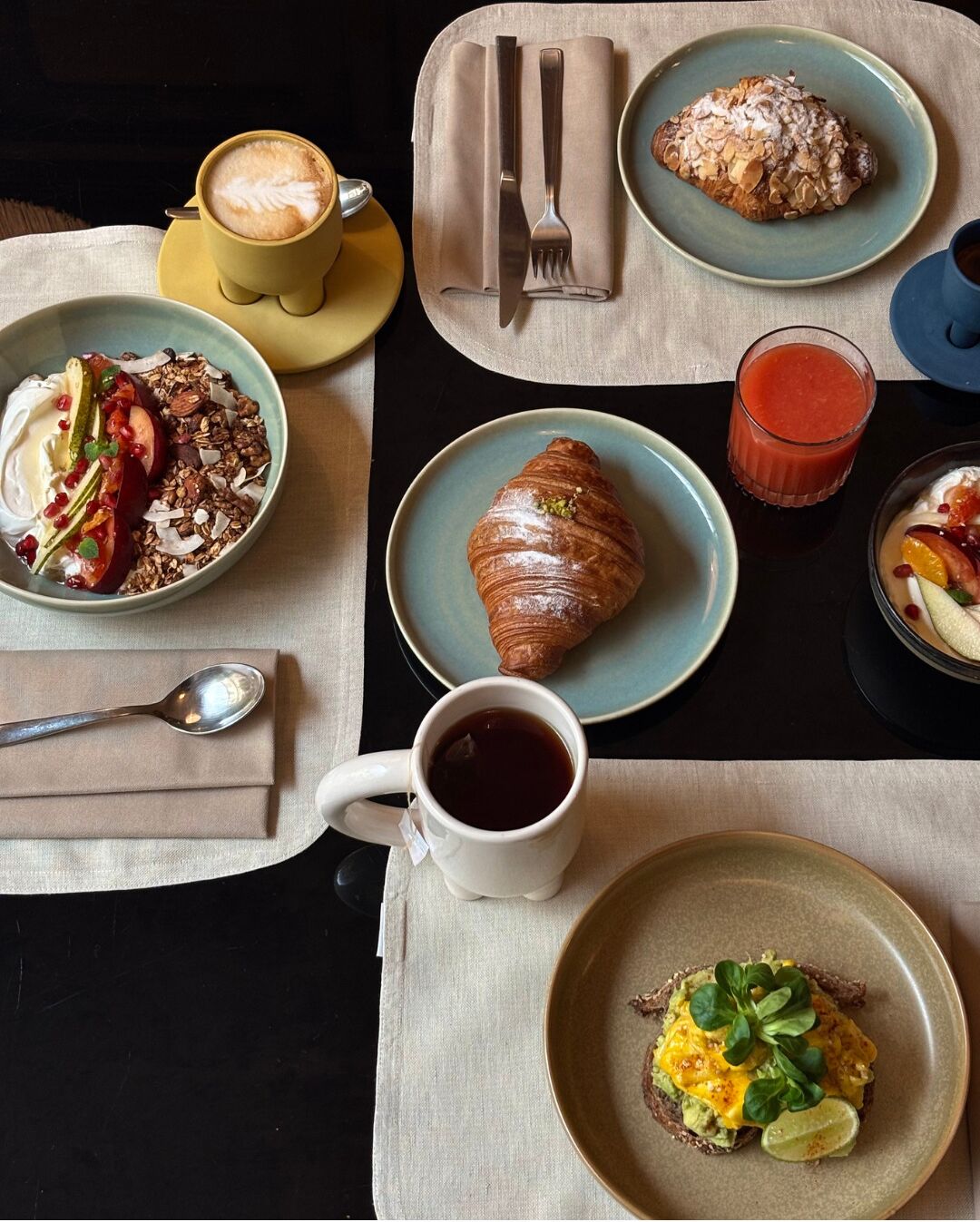 Ein Frühstückstisch mit Croissants, Kaffee, einem Smoothie und einem Joghurt mit Früchten und Granola.