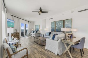 Un salon spacieux comprenant un canapé, une table basse et des fauteuils. Un téléviseur est fixé au mur, ainsi qu’un ventilateur de plafond et des œuvres d’art.