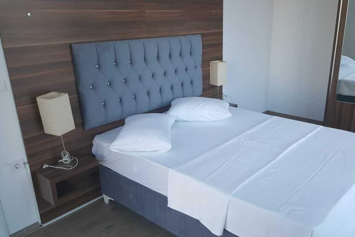 A neatly made bed with a tufted headboard, a bedside lamp, and a small wooden nightstand.