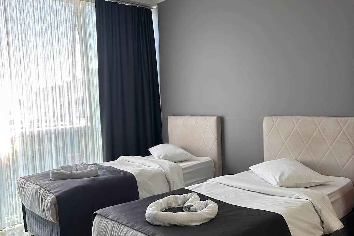 A modern hotel room with two beds, a large window with curtains, and a wooden floor.