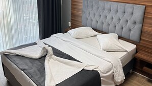 Ein modernes Hotelzimmer mit einem großen Bett, einem Holzkopfteil und Blick durch transparente Vorhänge.