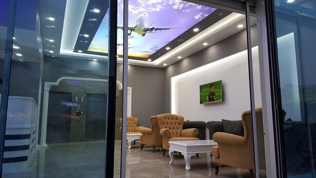 Ein stilvoller Lounge-Bereich mit bequemen Sitzmöglichkeiten, einem Fernseher, der ein Sportereignis zeigt, und einer Decke mit Himmel-Design.