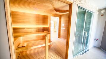 A sauna room with wooden benches and a glass door leading to a hallway.