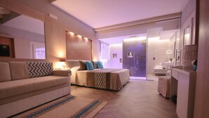 Una habitación de hotel moderna con sofá, cama con ropa de cama estampada, baño con espejo y lavabo, y suelo de madera.