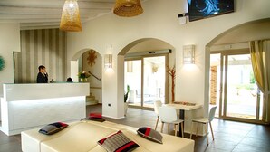 Un hall de hotel con una mesa de recepción, un amplio espacio de asientos con cojines y una mesa de comedor con sillas.