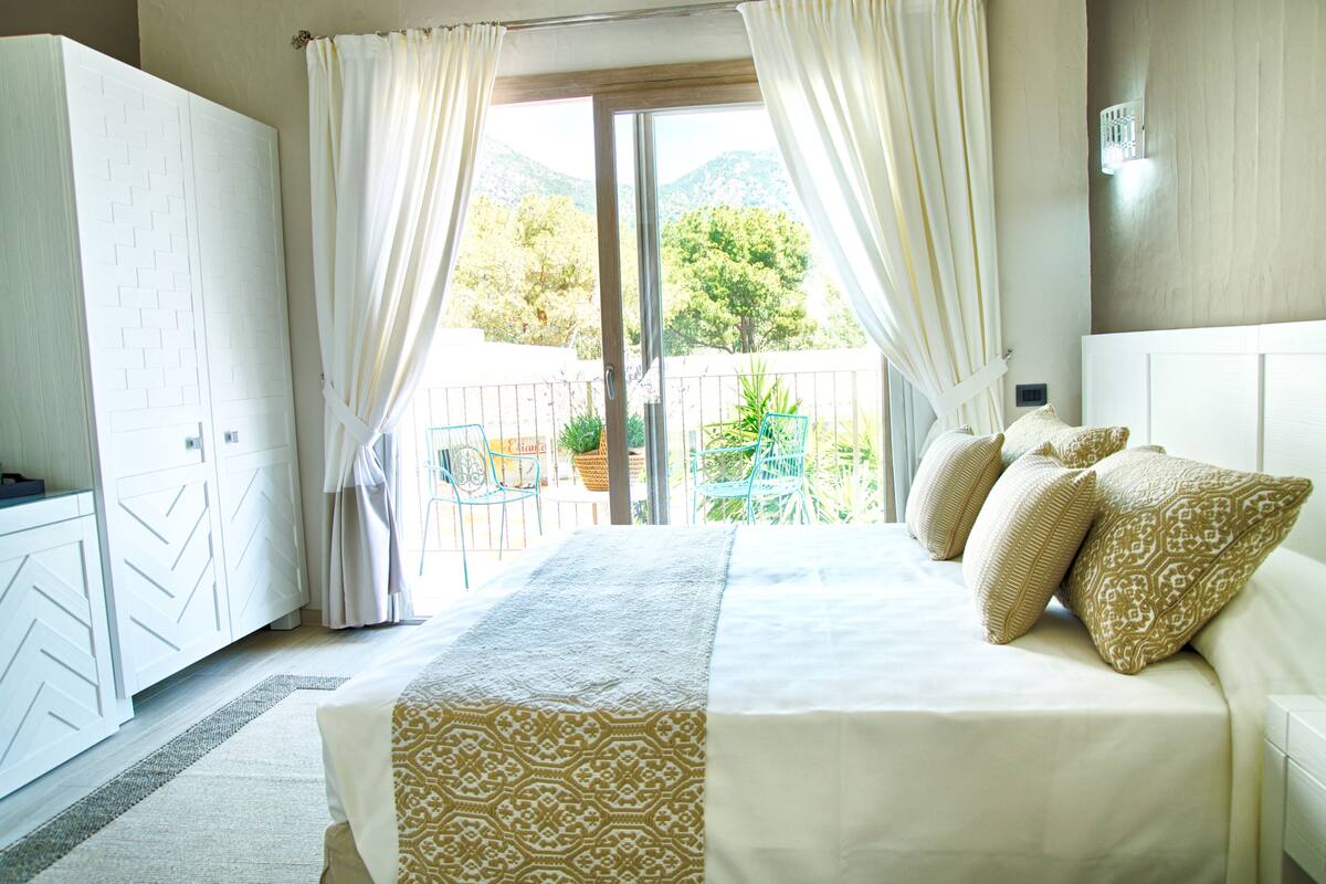 A bedroom with a large bed, a wardrobe, and a view of the outdoors.