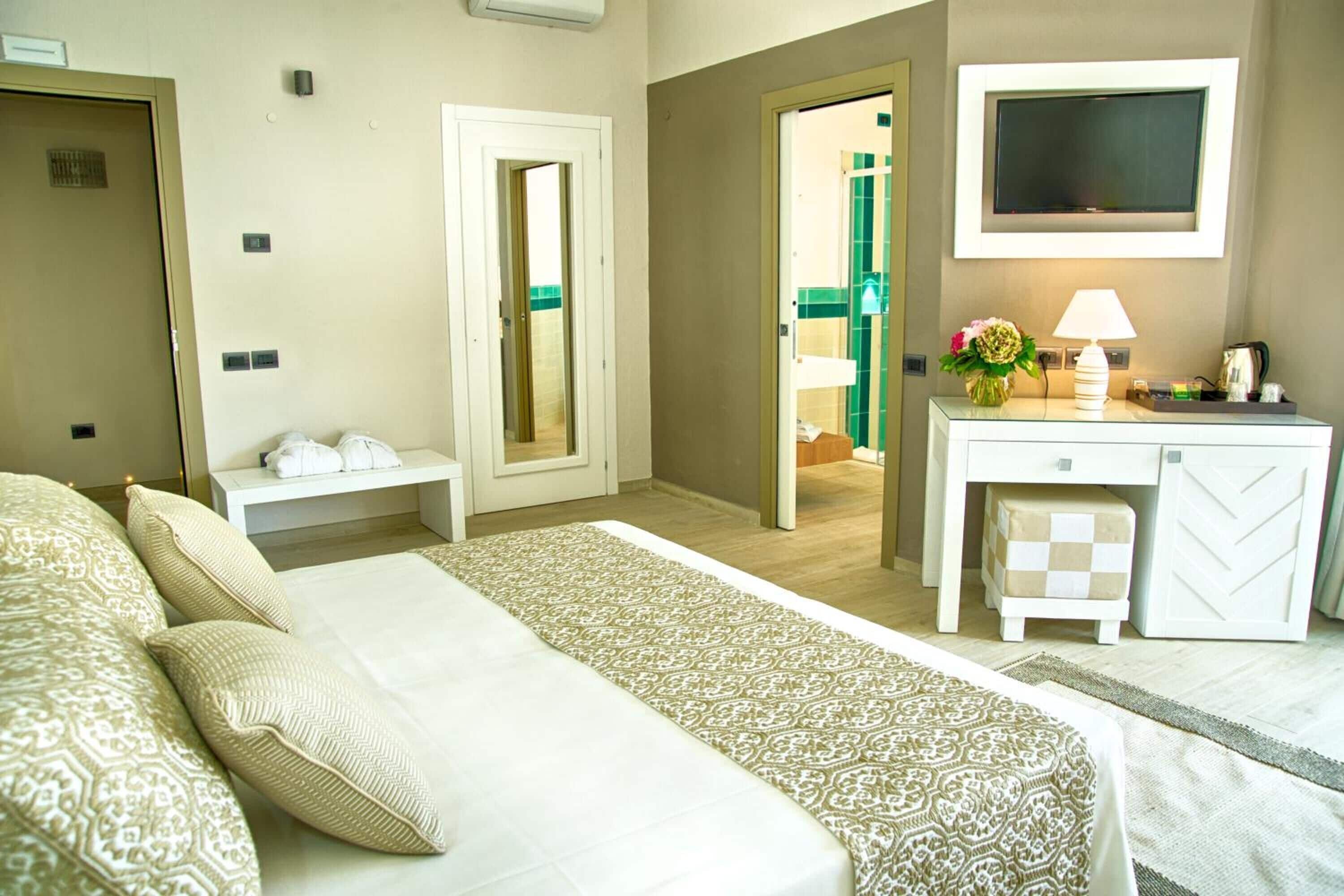 A hotel room with a bed, a desk, a TV, and a bathroom visible through an open door.