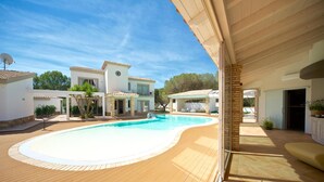 Una piscina con muelle de madera, un patio cubierto y un edificio blanco con tejado de baldosas.
