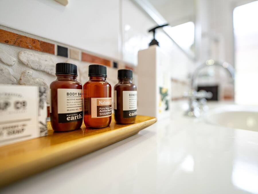 Three bottles of body care products on a wooden shelf in a bathroom.
