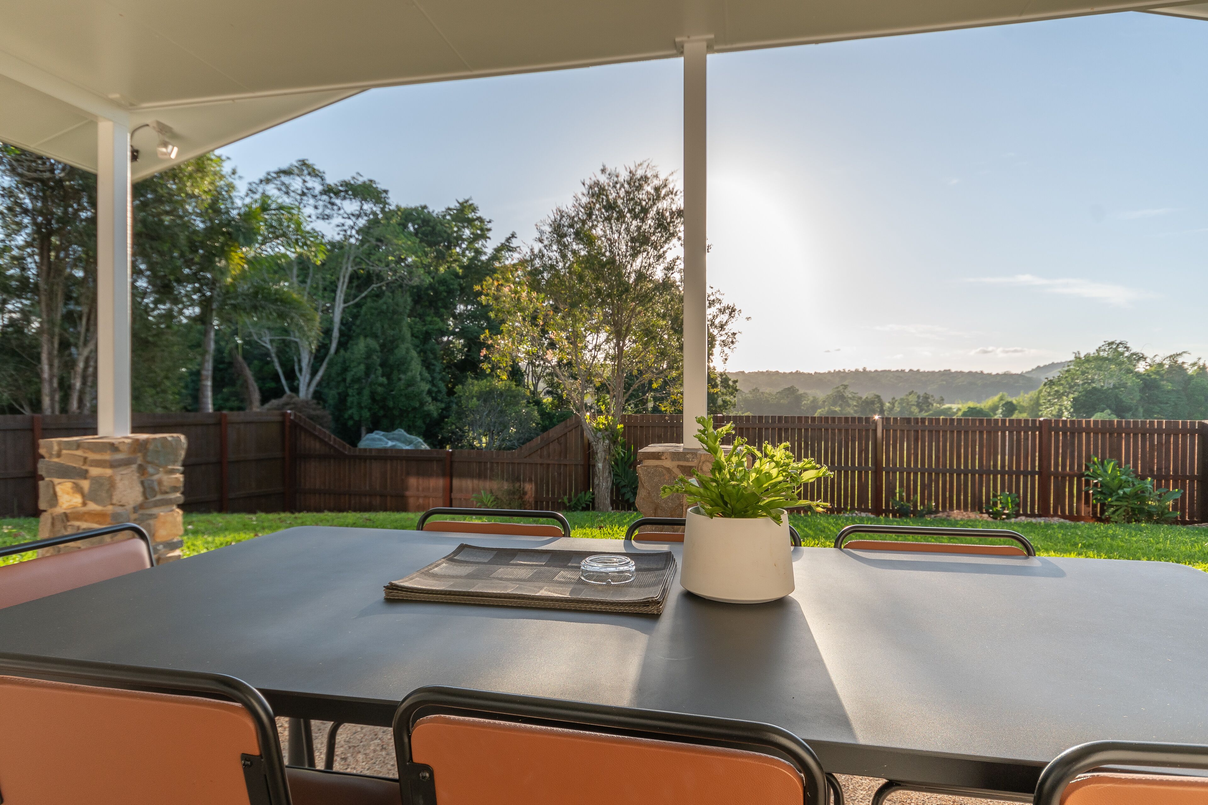 An outdoor patio with a table set for dining, surrounded by chairs, and a potted plant.