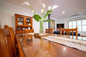 A dining table with chairs, a vase with flowers, a wooden cabinet, and a television in a room with a window.