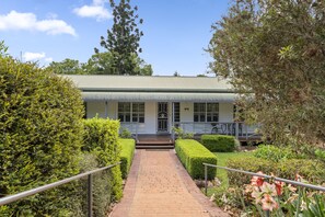 A building with a green roof, a brick pathway leading to the entrance, and well-maintained hedges. - Birds 'n' Bloom Cottages (Yungaburra)