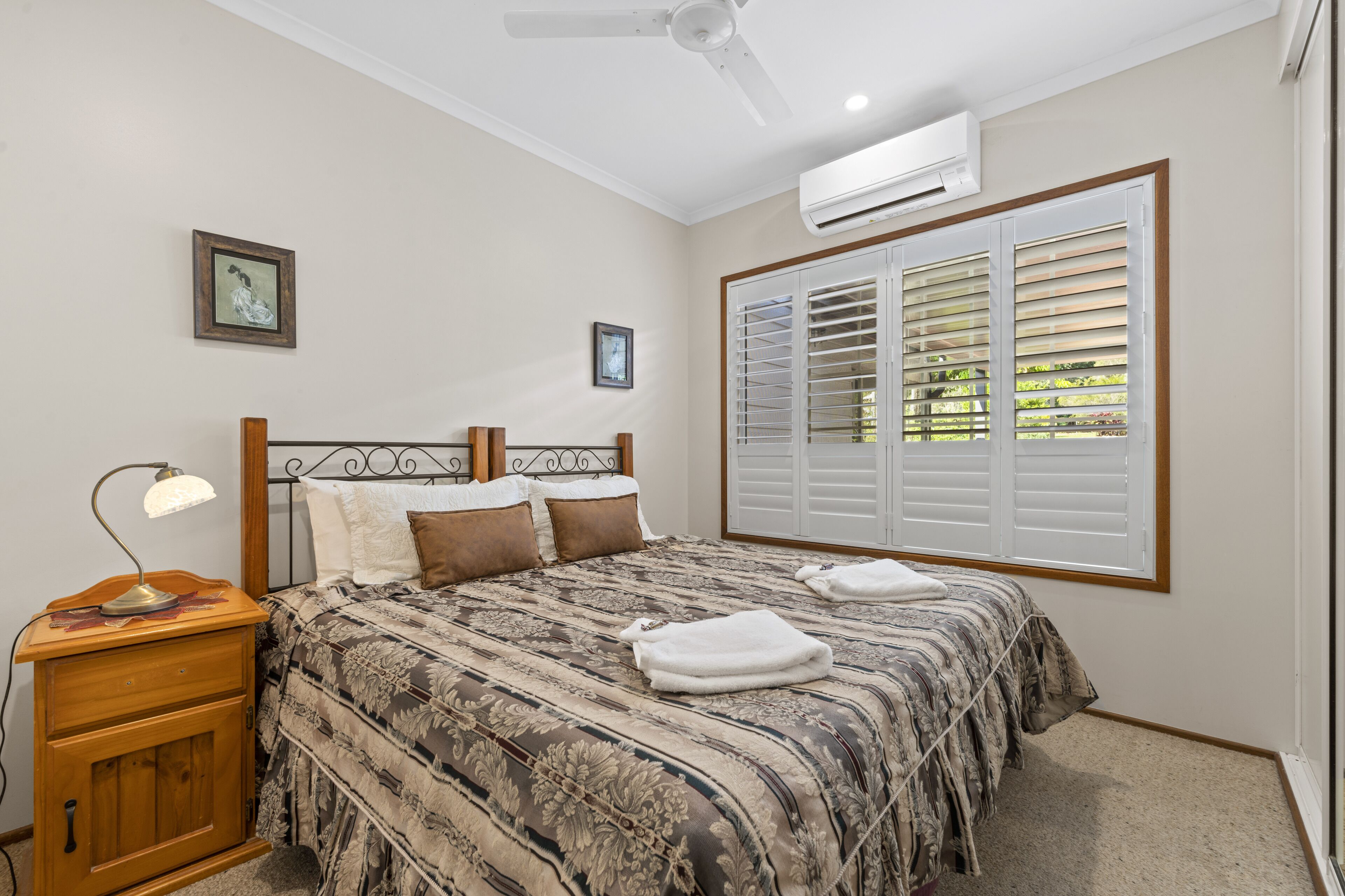 A bedroom with a bed, a nightstand, a ceiling fan, and a window with blinds.