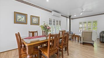 A dining area with a wooden table and chairs, framed pictures on the wall, and a window with blinds.